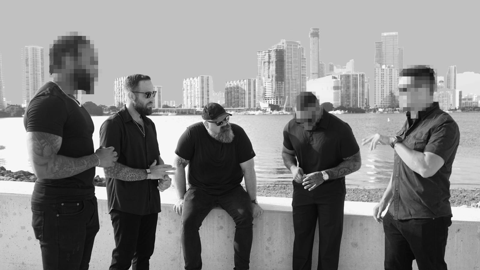 Miami Private Investigations team at Biscayne Bay wall with the Miami skyline behind them — operator identities redacted for client confidentiality